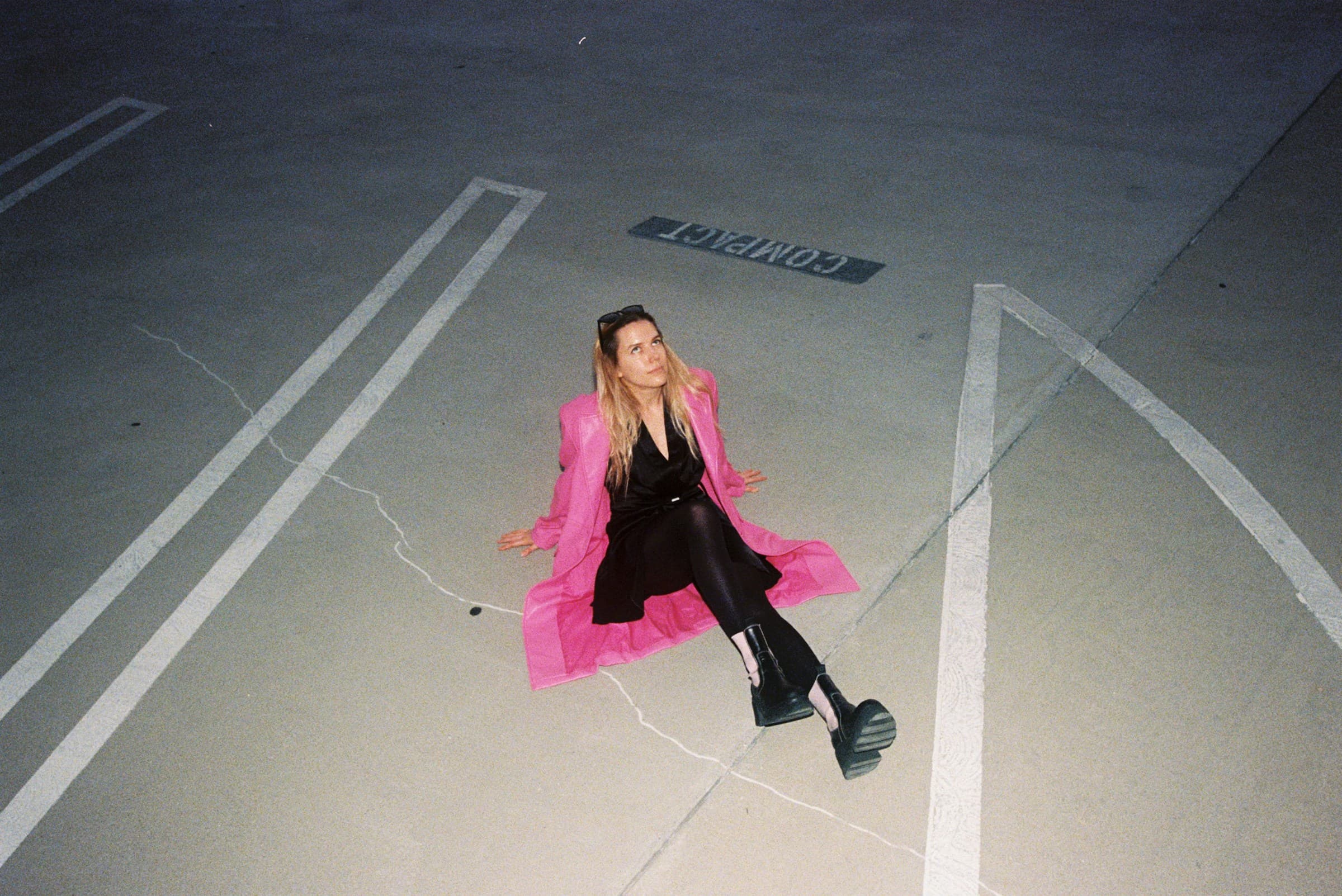 Woman in a hot-pink fur-trimmed coat lying on parking-lot markings at night
