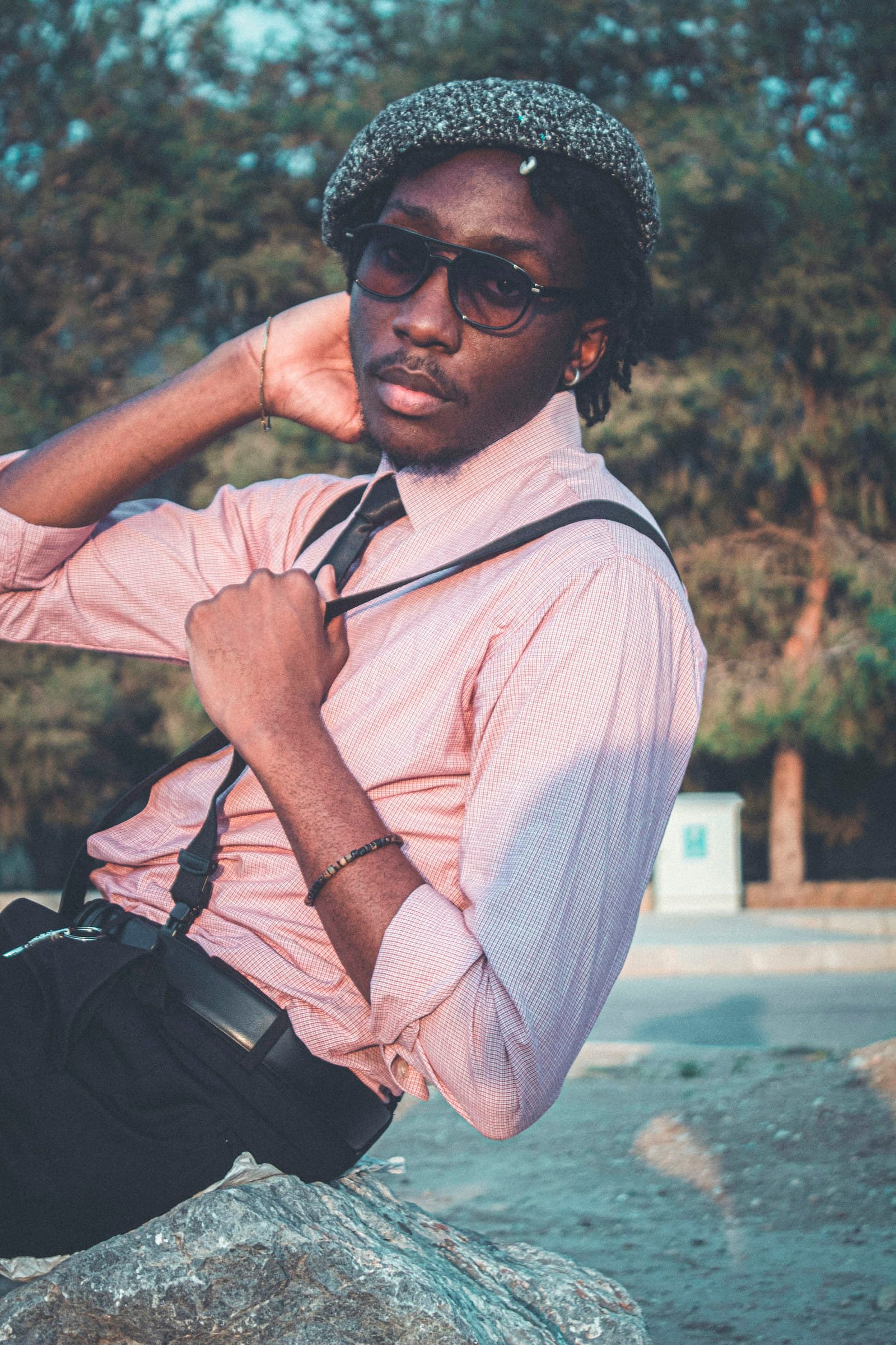 Young man in a pink shirt, cap, and suspenders posing outdoors